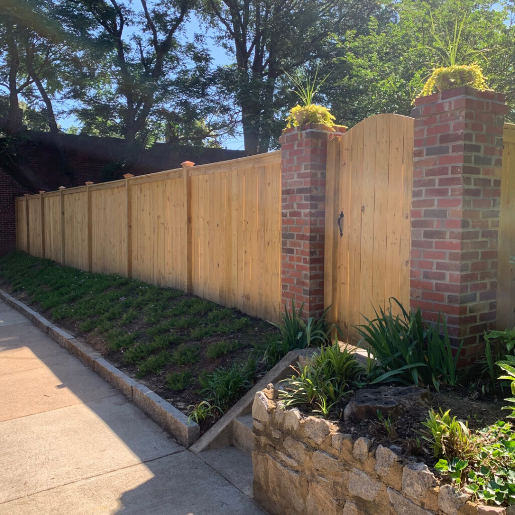 Six foot tall, top cap and finish board wood privacy fence featuring brick columns and arched gate.